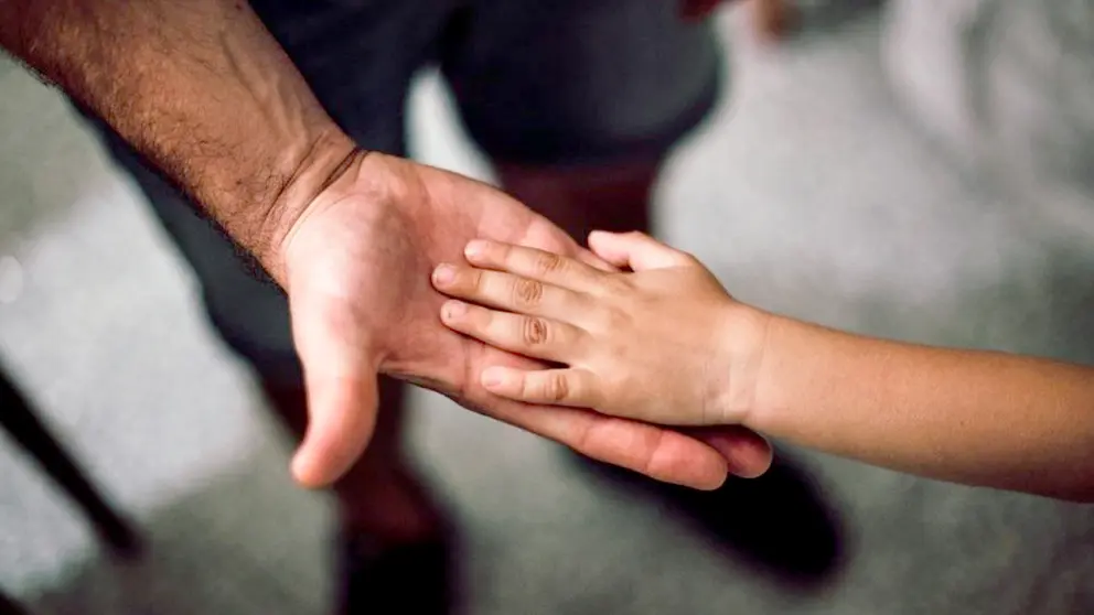 Fotografía ilustrativa de la mano de un adulto y una menor de edad. Pexels
