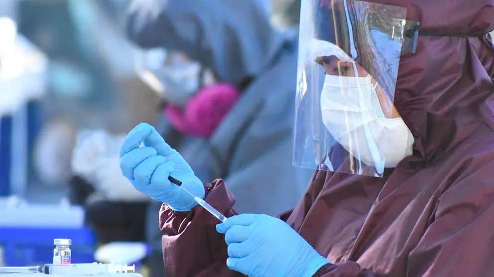 Personal de salud con un traje de bioseguridad alista una dosis para vacunar. Dico SolÍs