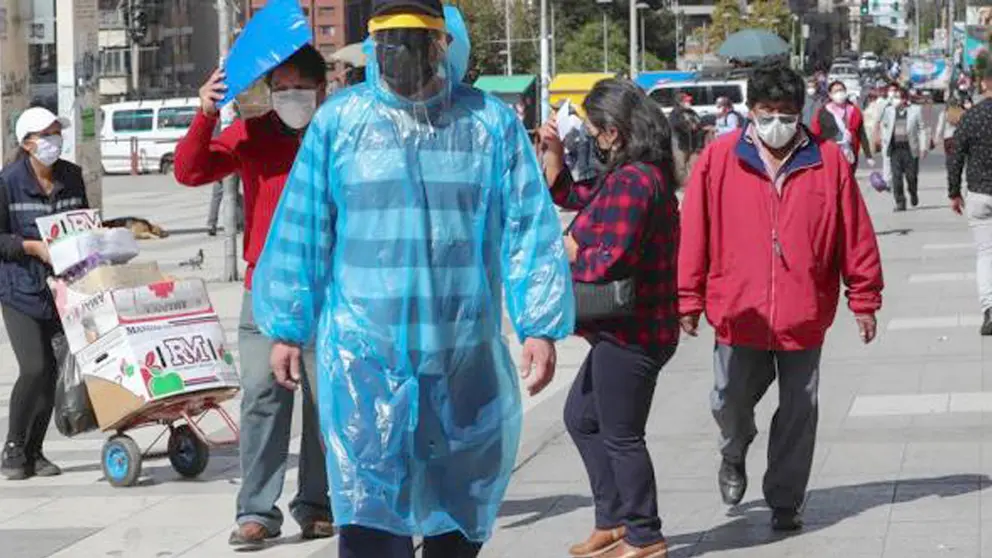 Peatones utilizando mascarillas y trajes de pl&aacute;stico para protegerse de la COVID-19 en La Paz. EFE