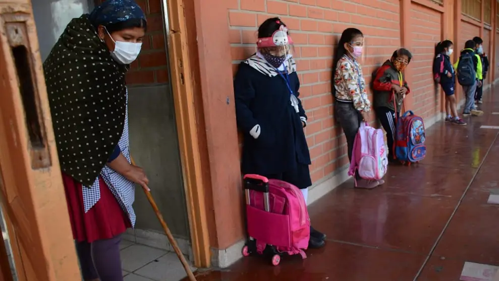 Una madre de familia desinfecta un aula, mientras los escolares hacen fila para ingresar. DICO SOLÍS