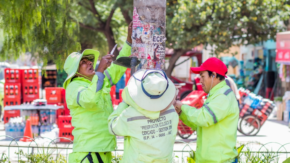 Trabajadores municipales limpian y retiran propaganda pol&iacute;tica de un poste en la ciudad. GAMC