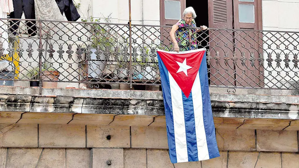 Una mujer sale al balcón donde se expone una bandera cubana en La Habana. EFE 