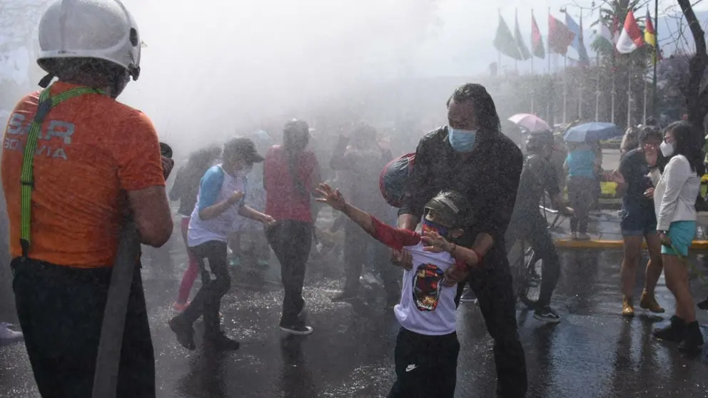 Un grupo de personas se refresca con los chorros de agua del carro bombero del grupo SAR Bolivia. Dico Sol&iacute;s