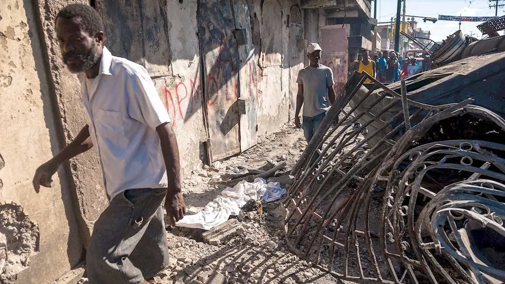 Dos hombres caminan junto a escombros y un cadáver descubierto por la comunidad tras la explosión este martes de un camión, hoy, en Cap-Haitien (Haití). EFE