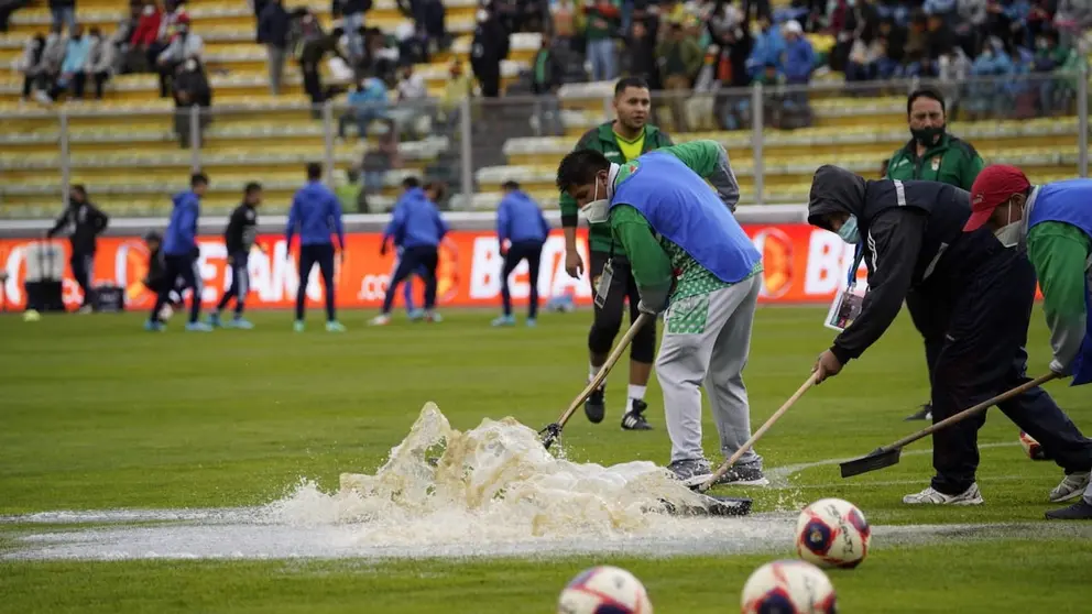 Funcionarios del Sedede de La Paz despejan el agua en el césped del estadio Hernando Siles mientras los seleccionados de Bolivia y Chile realizan labores precompetitivas. APG