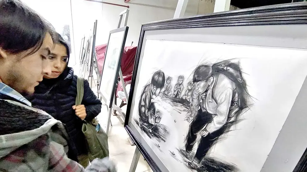 Dos espectadores  observan uno de los dibujos premiados./ DICO SOL&Iacute;S