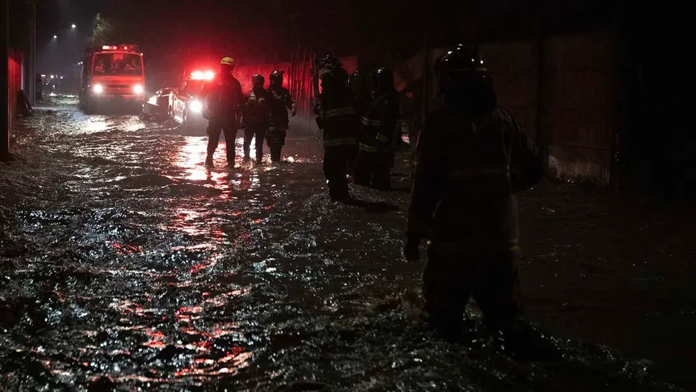 Bomberos caminan en la madrugada de hoy por calles anegadas por agua tras la crecida del r&iacute;o Cachapoal, producto de las intensas lluvias en la comuna de Coltauco (Chile). EFE