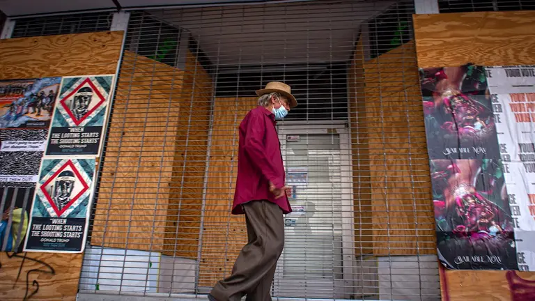 Un hombre camina delante de tiendas totalmente cubiertas con tablones de madera por temor a posibles ataques y protestas debido a las elecciones presidenciale, en el centro de Miami. EFE