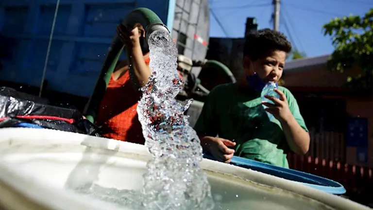 Una ni&ntilde;a en El Salvador llena un balde con una manguera. EFE