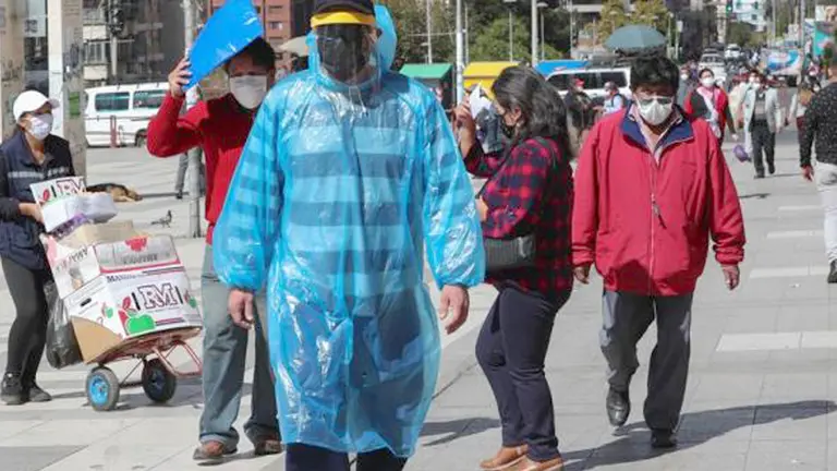 Peatones utilizando mascarillas y trajes de pl&aacute;stico para protegerse de la COVID-19 en La Paz. EFE