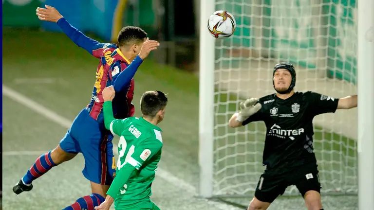 El defensa del FC Barcelona Ronald Araújo (i) cabecea un balón ante Gerard Martín (c) y el portero Ramón Juan, ambos del Cornellá. EFE