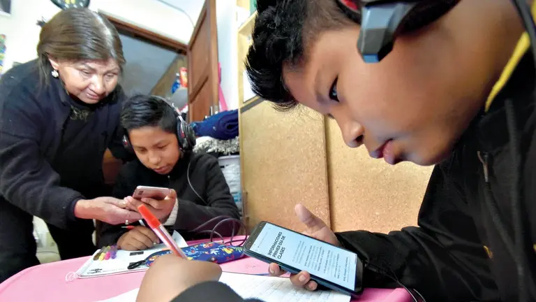 Dos niños pasan clases virtuales en su casa con un familiar.  APG