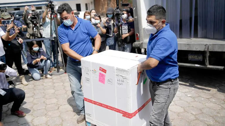 Dos hombres bajan de un cami&oacute;n una caja que contiene dosis de las vacunas, en 
El Salvador. EFE