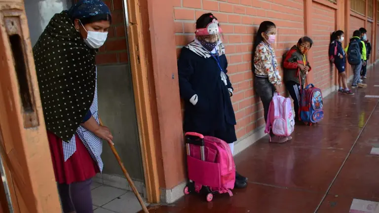 Una madre de familia desinfecta un aula, mientras los escolares hacen fila para ingresar. DICO SOLÍS