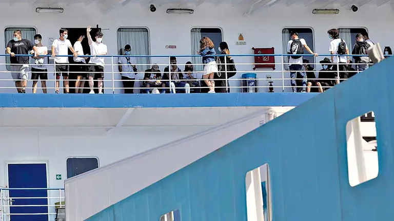 Varias personas saludan desde el ferry en el que viajan 118 estudiantes. EFE