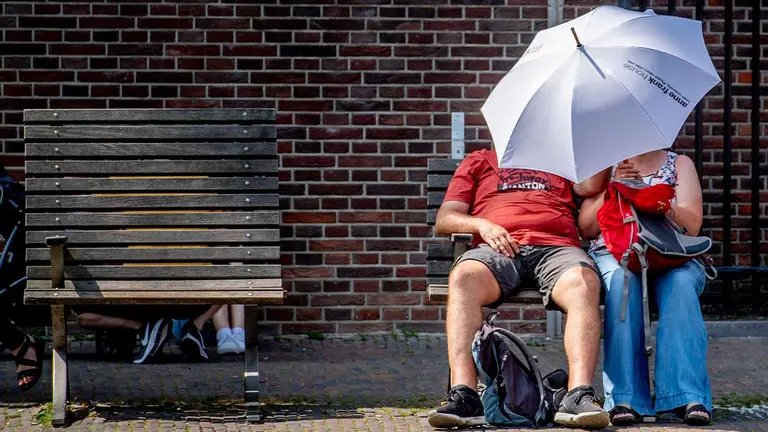 Fotografía de dos personas en una banca en Toronto, cubriendo sus rostros del sol. EFE