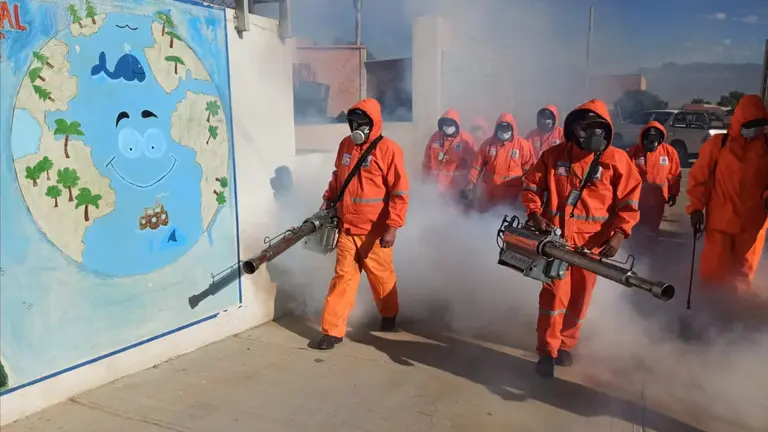 Trabajadores de EMSA realizan la fumigaci&oacute;n en la Unidad Educativa Voces Libres. GAMC