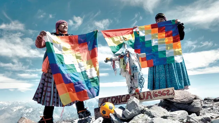 Dos cholitas muestran la whipala, la bandera de los pueblos indígenas andinos, en la cima del Aconcagua.     ARENA COMUNICACIÓN