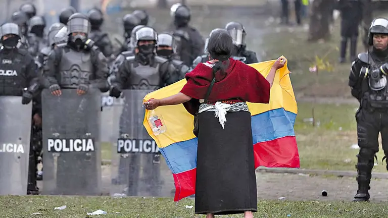 Una mujer indígena levanta una bandera frente a un grupo de policías. EFE