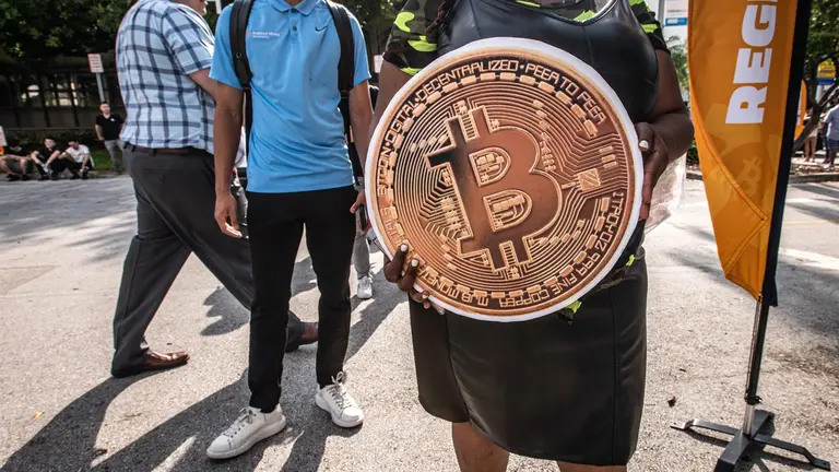 Una persona sostiene una enorme bitcoin mientras espera en fila para entrar a la conferencia Bitcoi.     EFE