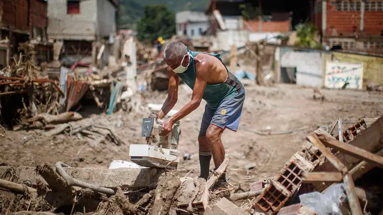 Personas buscan objetos para rescatar entre los escombros tras derrumbes provocados por las fuertes lluvias, hoy, en Las Tejer&iacute;as (Venezuela). EFE
