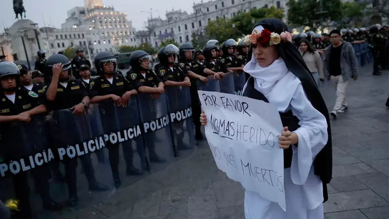 Una mujer con un cartel con un mensaje de paz camina frente a polic&iacute;as en Per&uacute;./ EFE