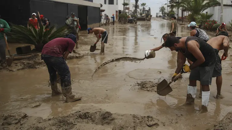 Personas ayudan a remover el lodo en una calle afectada por las lluvias, en el balneario de Punta Hermosa al sur de Lima (Per&uacute;), en una fotograf&iacute;a de archivo./ EFE