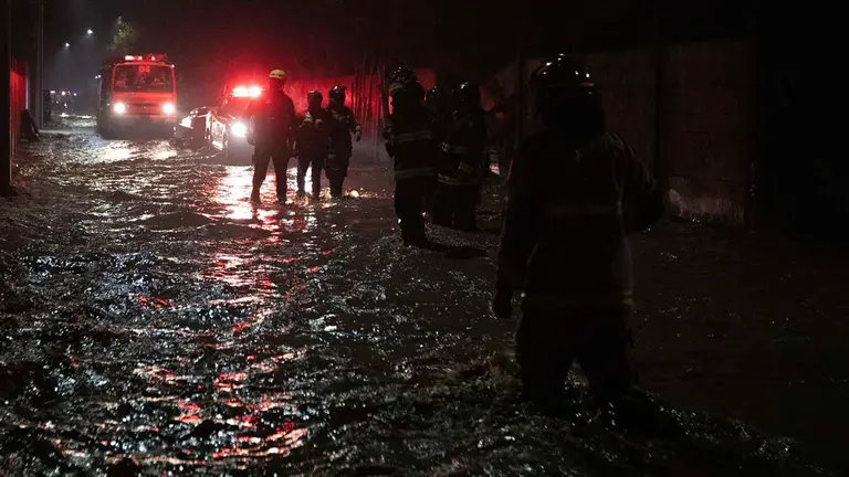 Bomberos caminan en la madrugada de hoy por calles anegadas por agua tras la crecida del r&iacute;o Cachapoal, producto de las intensas lluvias en la comuna de Coltauco (Chile). EFE