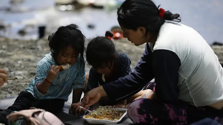 Una migrante ecuatoriana come junto a sus hijas en la selva mientras esperan para ser trasladados en canoa en Bajo Chiquito, Dari&eacute;n (Panam&aacute;), en una fotograf&iacute;a de archivo./ EFE
