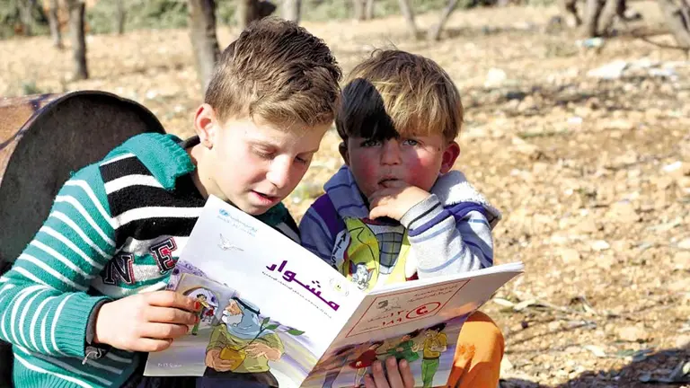 Ni&ntilde;os de Siria leen un libro en un espacio abierto./ 20MINUTOS.ES