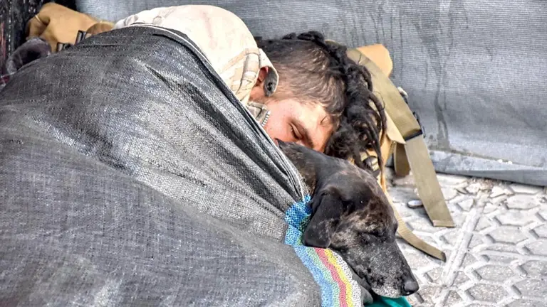 Una persona en situaci&oacute;n de calle se cobija de fr&iacute;o con su mascota./ DICO SOL&Iacute;S